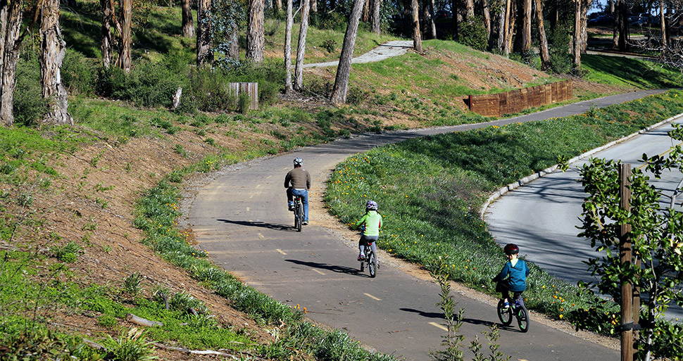 A man and two children cycle along a tree-lined bicycle path in San Mateo County